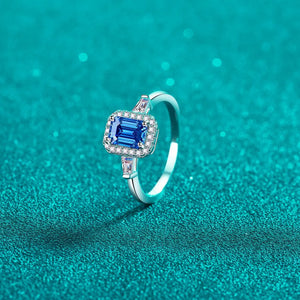 Emerald cut royal blue moissanite halo ring in sterling silver with baguette accents.
