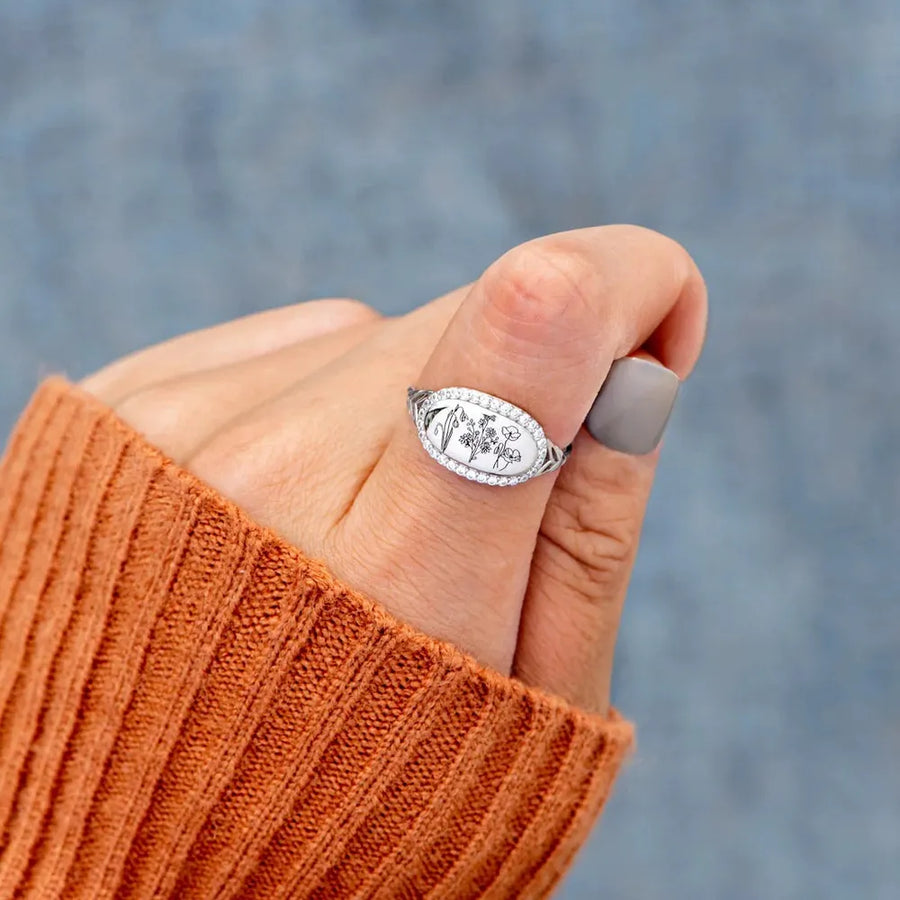 Silver engraved floral signet ring with diamond accents on a hand.