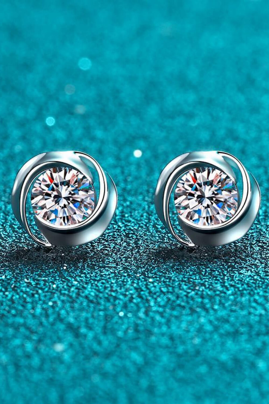 Silver halo stud earrings with clear crystals on a textured blue background.