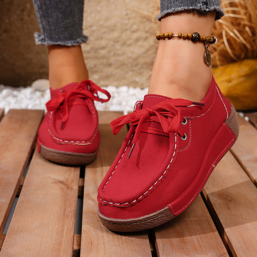 Red lace-up moccasin style sneakers with white stitching detail and a brown sole.