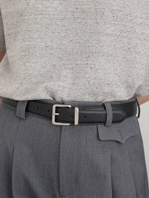 Black leather belt with elegant silver buckle, styled with grey trousers.