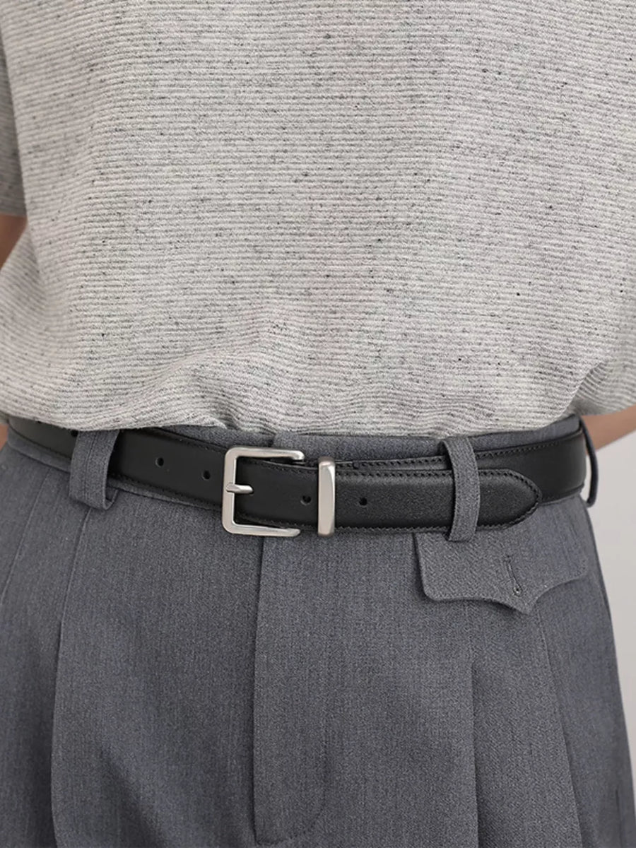 Black leather belt with elegant silver buckle, styled with grey trousers.