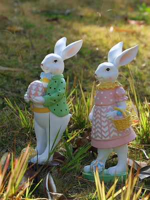 Easter bunny figurines, one in a green polka dot jacket, the other in a pink dress, holding eggs and a basket.