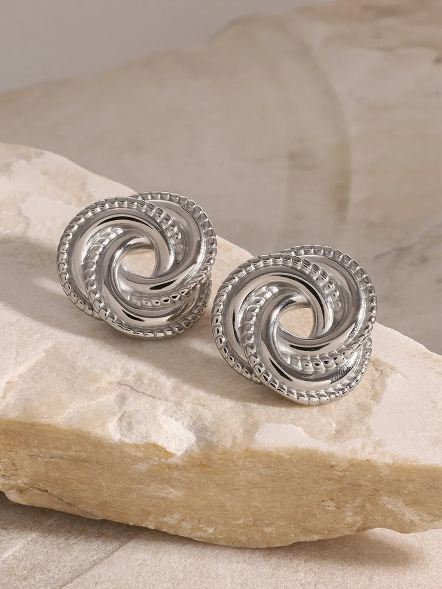Silver swirl knot stud earrings with textured rope edge detail.