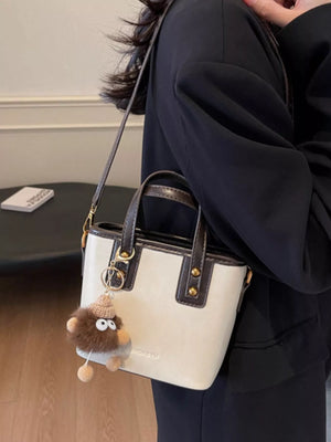 Mini leather crossbody bag in beige with dark brown trim and a fuzzy charm.