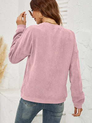 Dusty Pink corduroy sweatshirt with crewneck and long sleeves, styled with jeans.