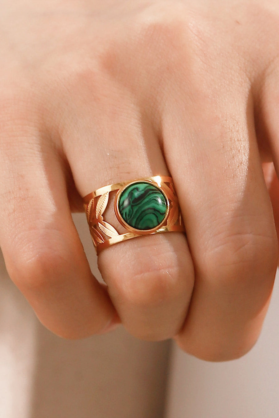 Gold ring with malachite stone and leaf cutouts on a finger