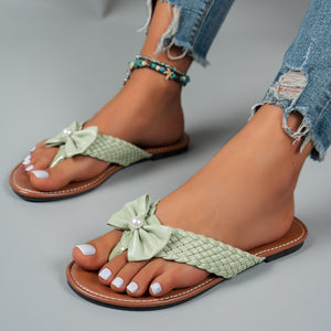 Green bow-embellished flat sandals with woven straps and pearl detail.