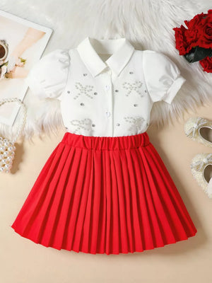 Girls' white bow-embellished top with puff sleeves and red pleated skirt.