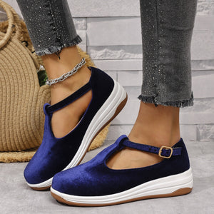 Blue velvet T-bar flat slip-ons with adjustable strap and white sole.