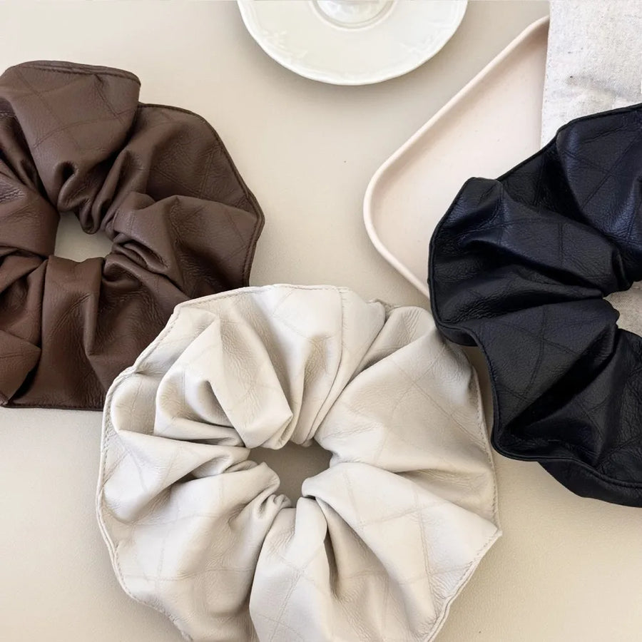Quilted faux leather scrunchies in beige, brown, and black with a diamond pattern.