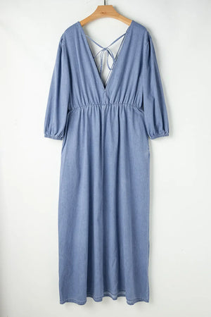 Light denim maxi dress with V-neck, cinched waist, puff sleeves, and tie-back detail.