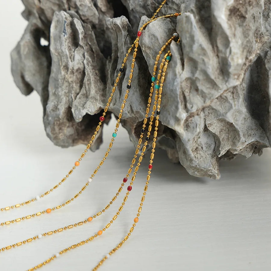 Gold necklaces with colorful beads and gold bar accents cascade down, featuring red, black, white, orange, and turquoise