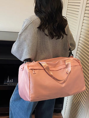 Pink duffel bag with adjustable strap and top handles, worn by a person in a grey sweatshirt.