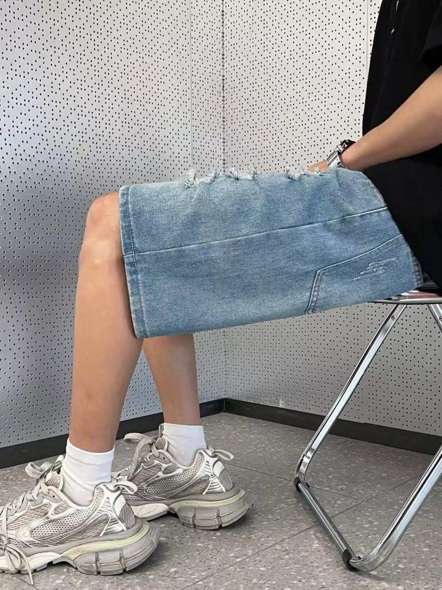 Men's light wash distressed denim shorts with wide leg and raw hem.