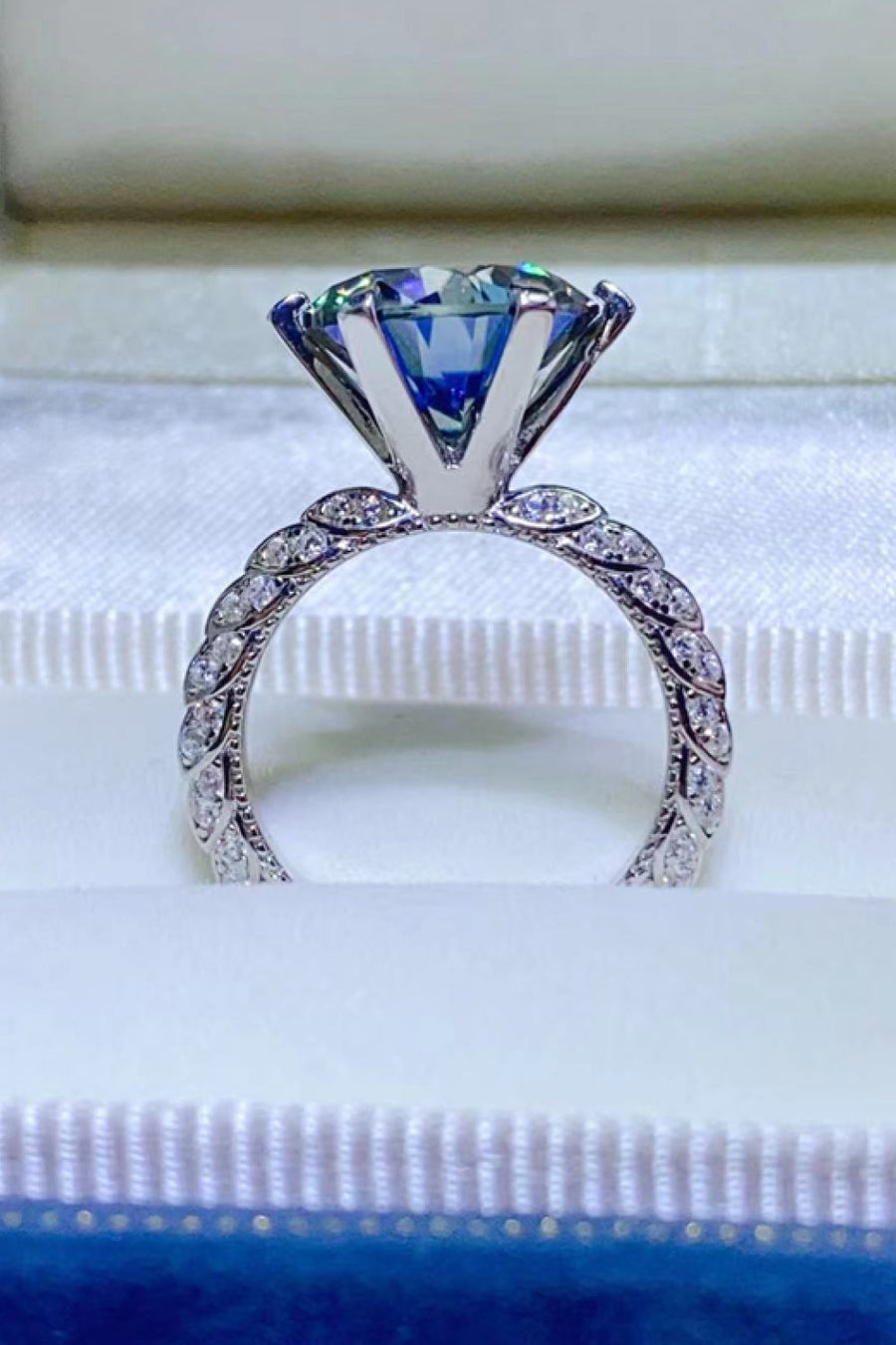 Blue solitaire engagement ring with pavé band and large faceted blue gemstone.
