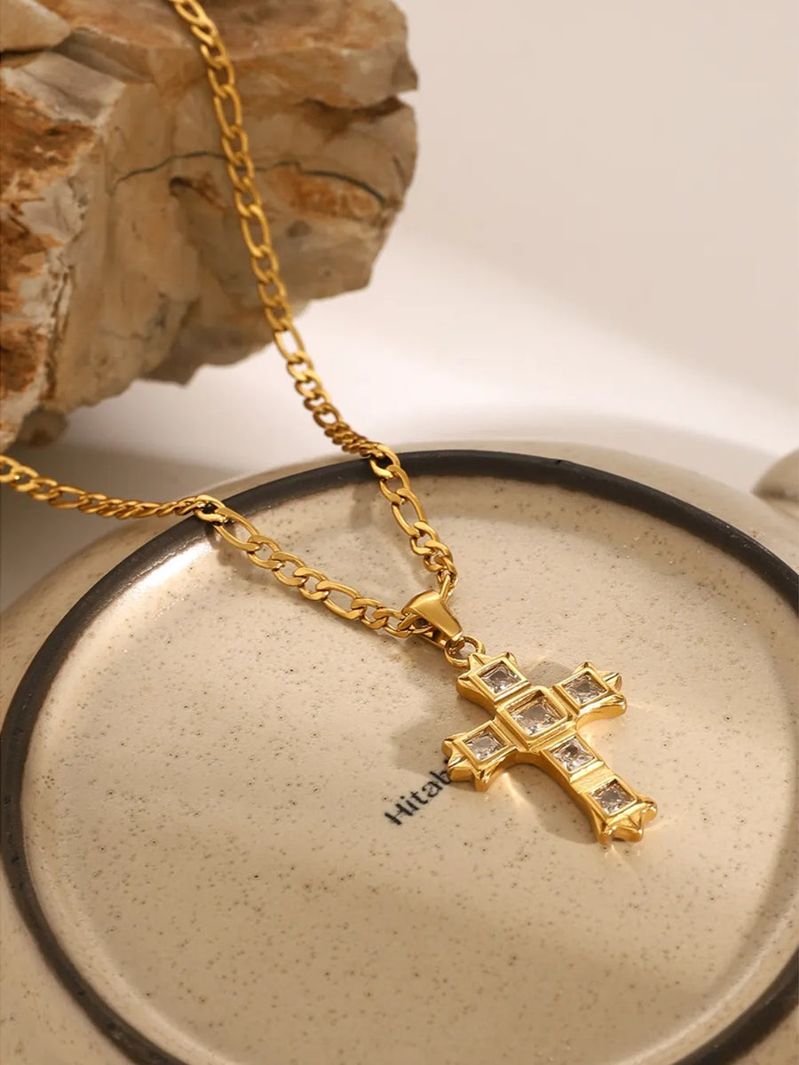 Gold cross pendant necklace with clear zirconia stones on a figaro chain.