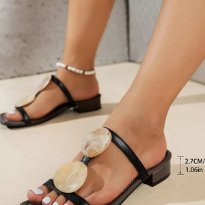 Black open-toe block heel sandals with decorative oval accents and a pearl anklet.