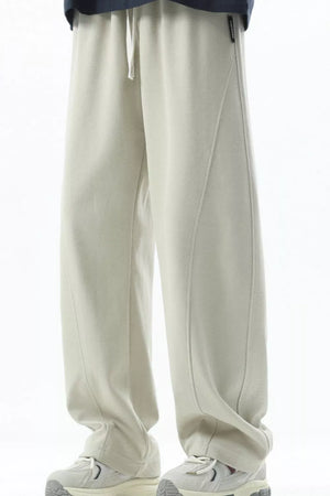 Men's beige loose fit sweatpants with drawstring and curved seam detail.