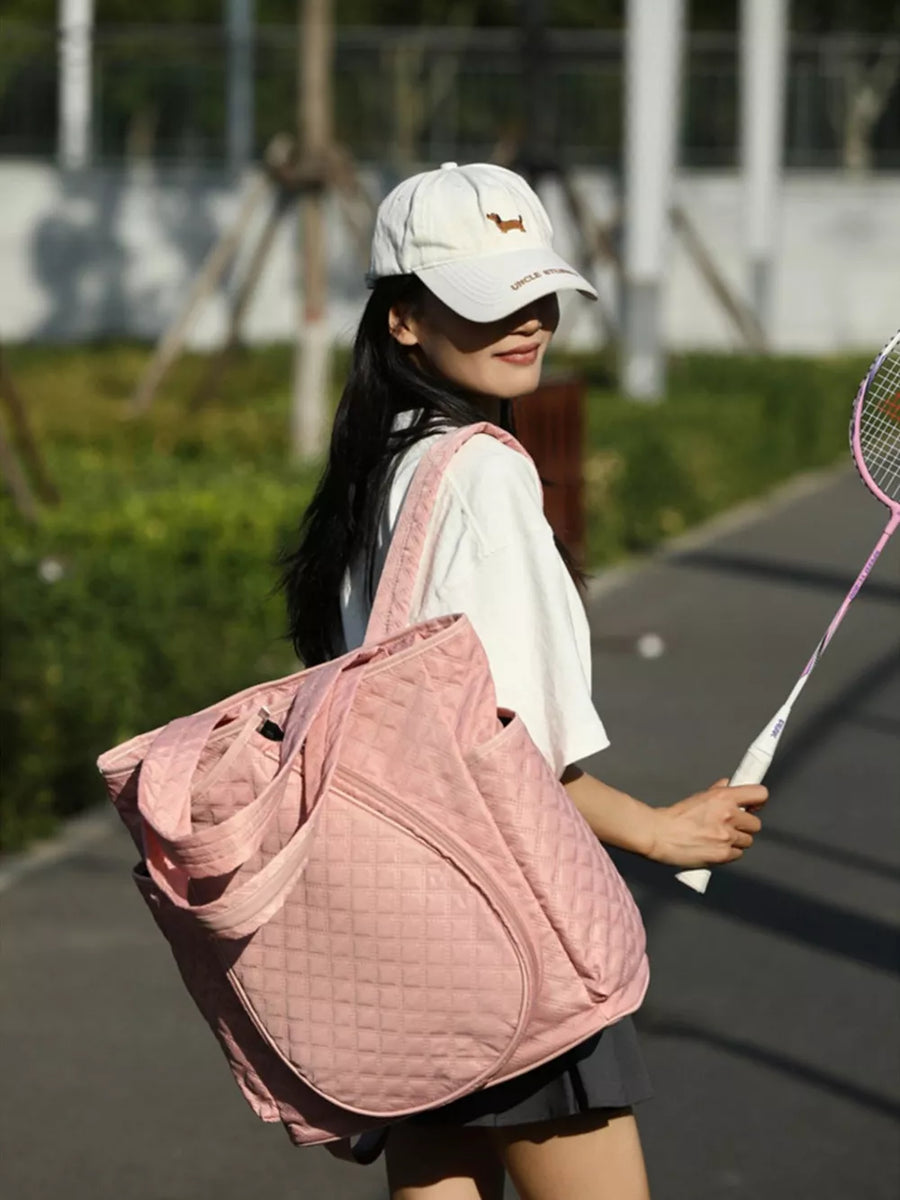 Pink quilted sports racket backpack with diamond pattern and zip pockets.