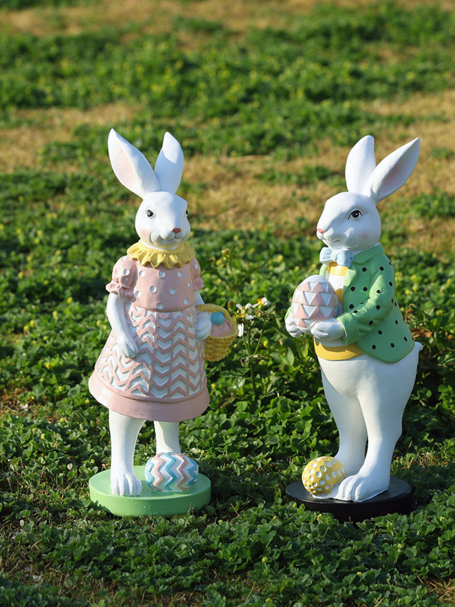 Easter bunny figurines in blush pink and gum leaf green holding eggs and baskets.