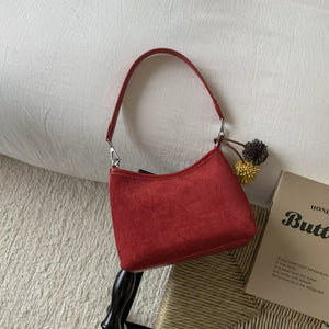 Red suede crossbody bag with charm detail and adjustable strap