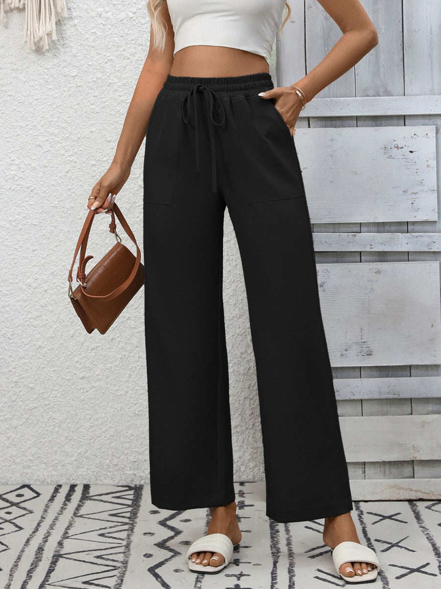 Black relaxed drawstring wide-leg pants with pockets, styled with a white crop top and brown bag.