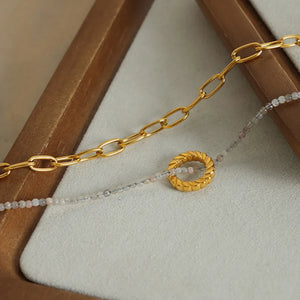 Gold layered chain necklace with beaded strand and twisted ring pendant.