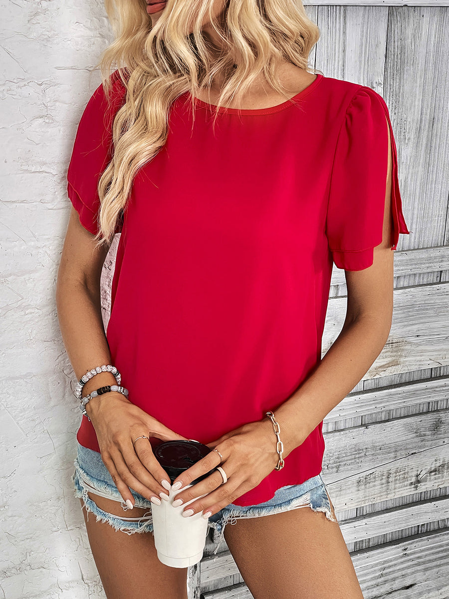 Red blouse with slit sleeves and a round neckline, styled with denim shorts.