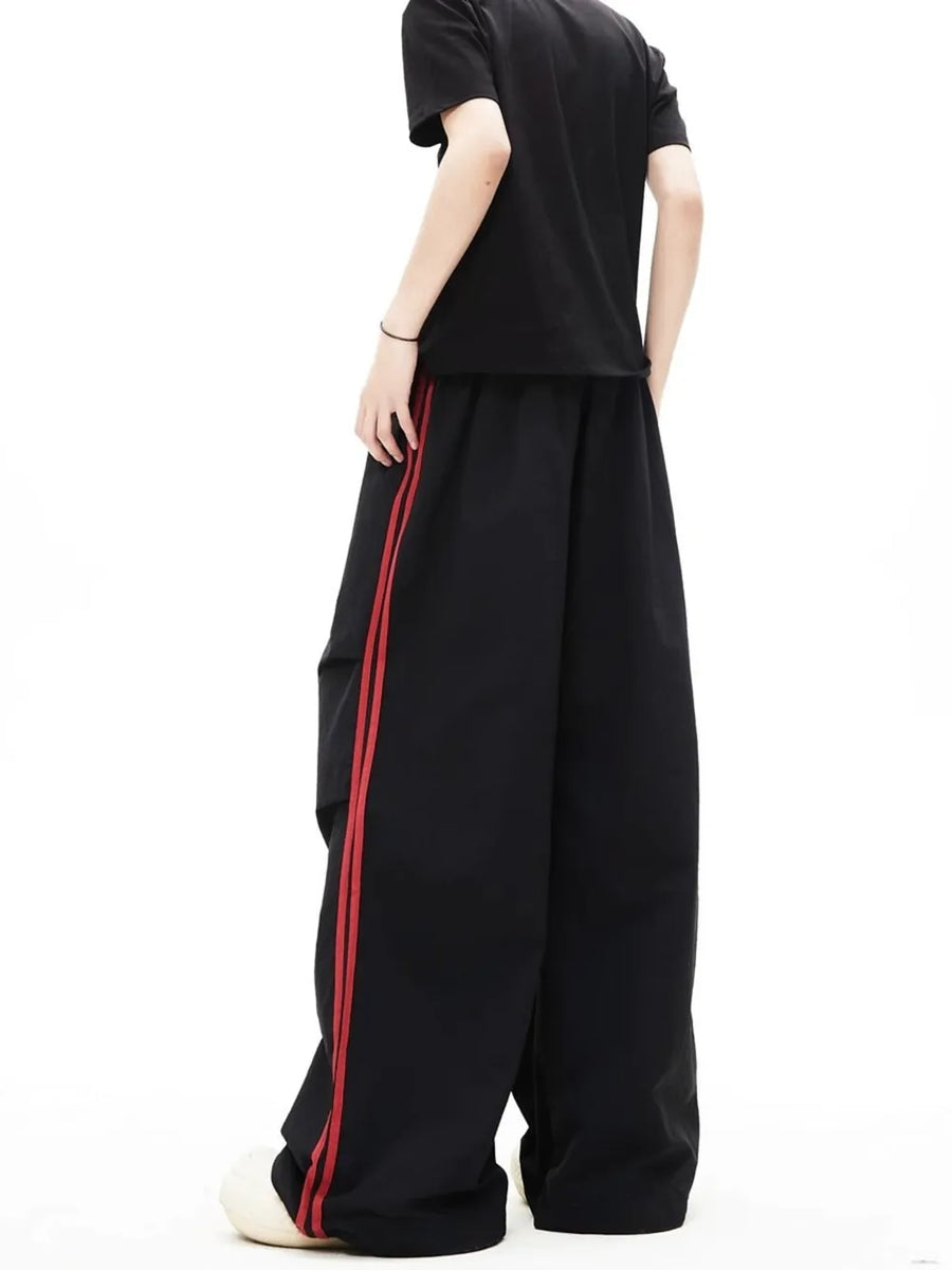 Black relaxed wide-leg sweatpants with red side stripes and contrast stitching.