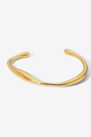 Gold open-ended bangle bracelet with a sculpted, fluid design.