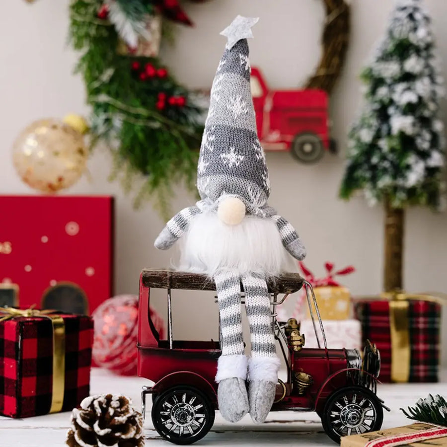 Illuminated knit gnome in gray with snowflake pattern, white beard, and striped legs sits on a red toy car.