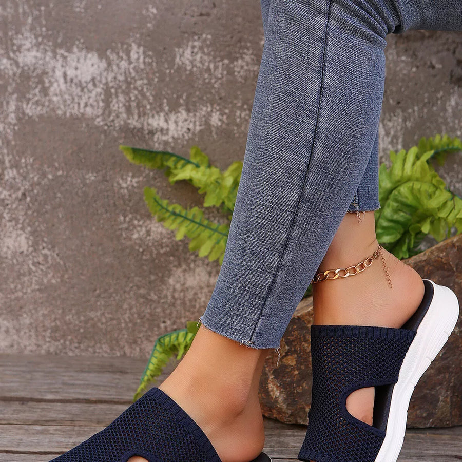 Dark blue mesh slip-on sandals with open toe and white sole, styled with jeans and a gold anklet.