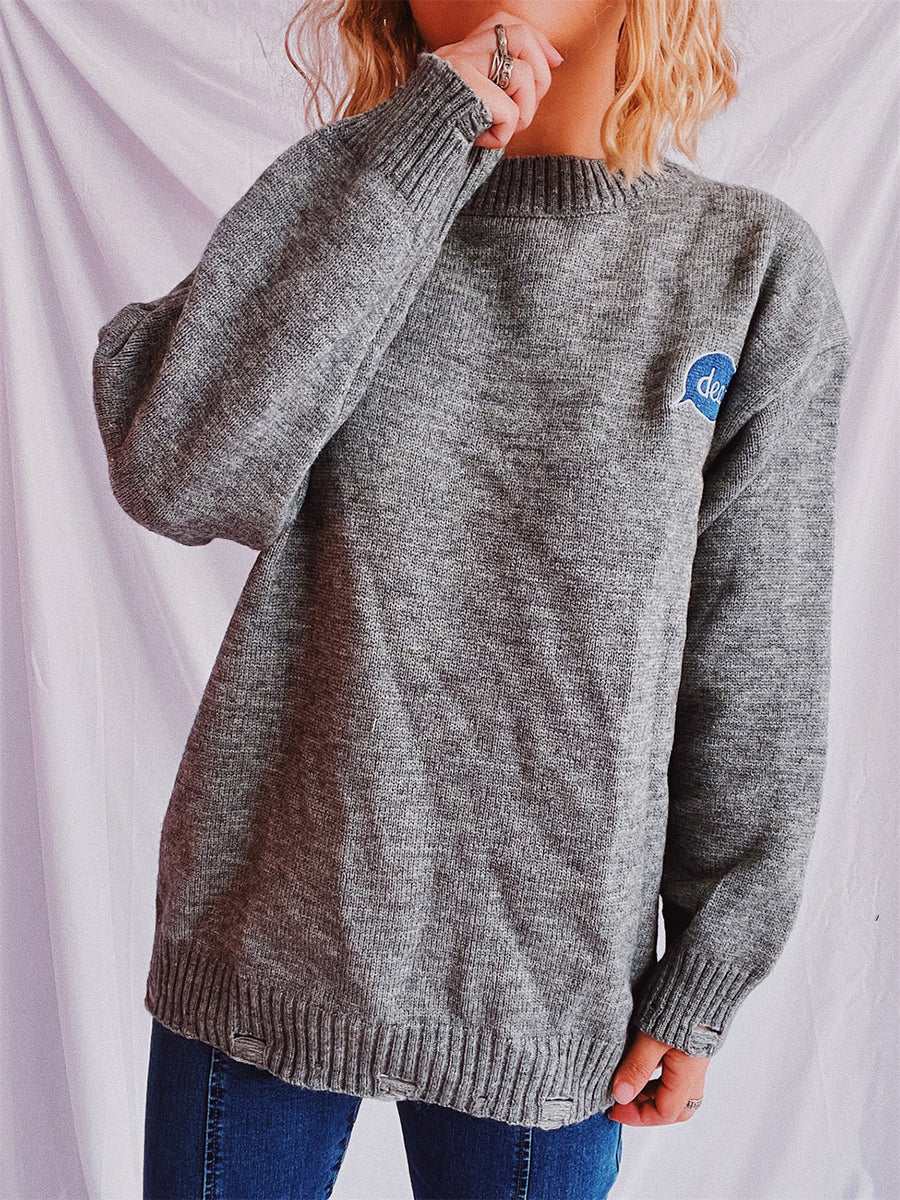 Dark gray relaxed knit sweater with embroidered blue speech bubble detail on chest.