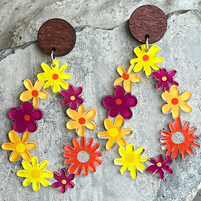 Floral wreath dangle earrings with wood tops, featuring colorful acrylic flowers in yellow, orange, and purple.