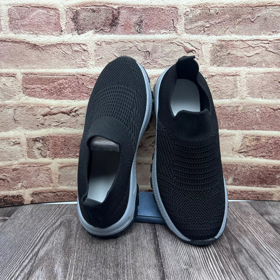 Black breathable round toe slip-on sneakers with a knit upper and grey sole.