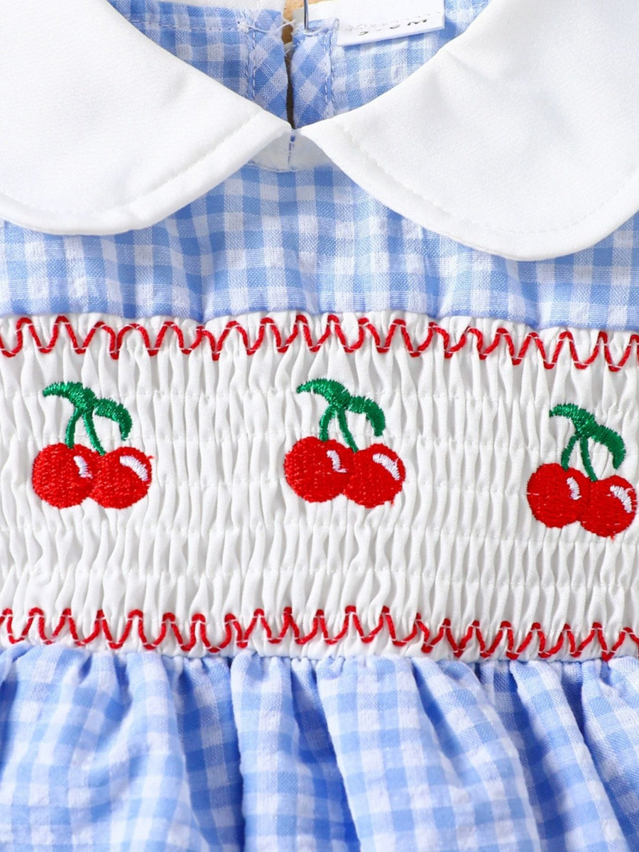 Baby dress in pastel blue gingham with smocked white bodice featuring embroidered cherries and a white collar.