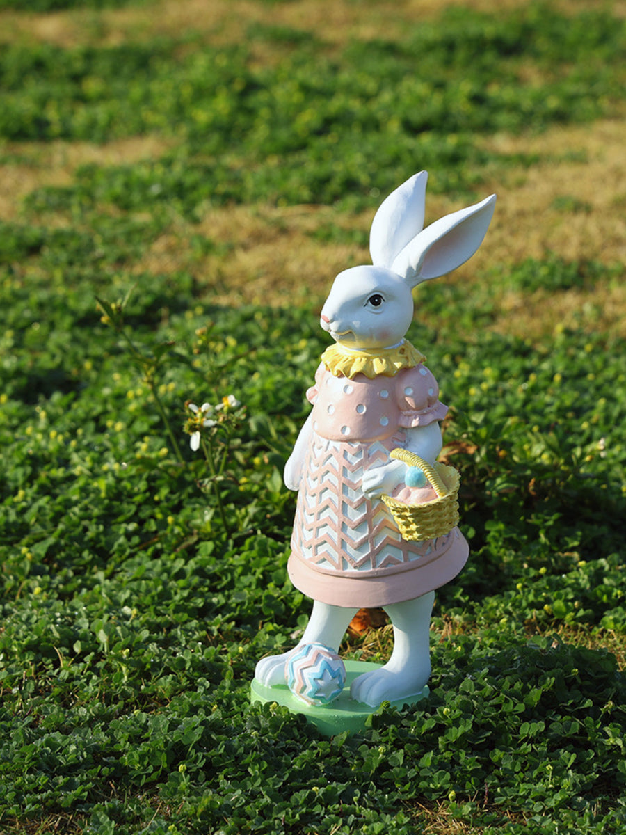 Easter bunny figurine in blush pink dress holding a basket of eggs, with patterned shoes.