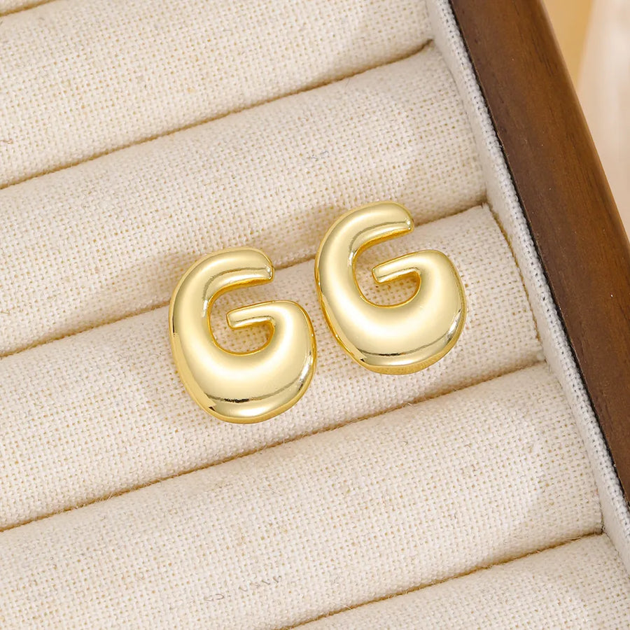 Gold sculptural stud earrings in the shape of the letter G.