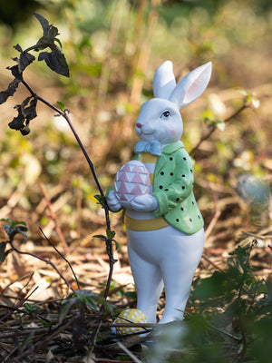 Easter bunny figurine in green polka dot jacket holding pink patterned egg, with yellow accents.