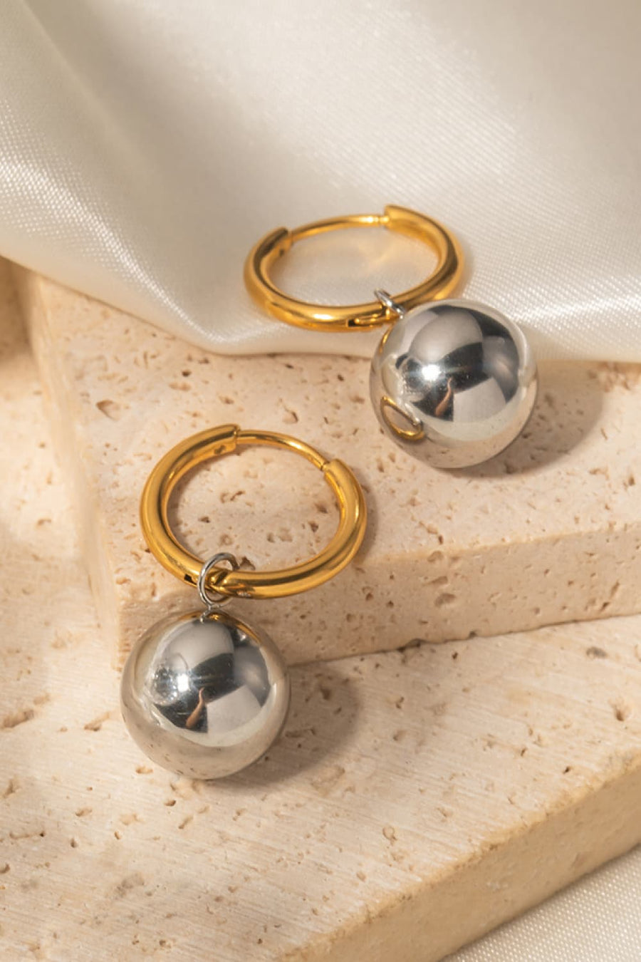 Orbital gold hoop earrings with dangling silver spheres.