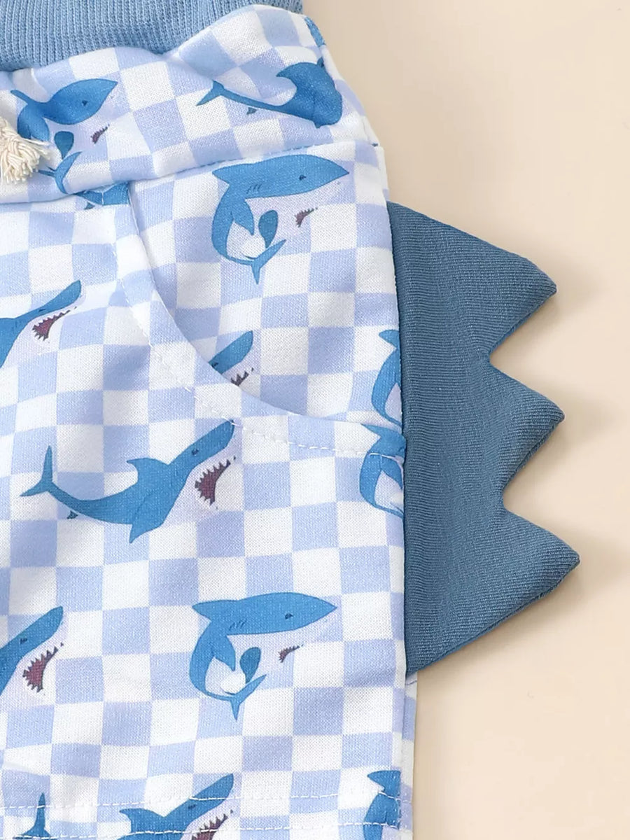 Baby blue checkered shorts with blue shark print and dinosaur tail detail.