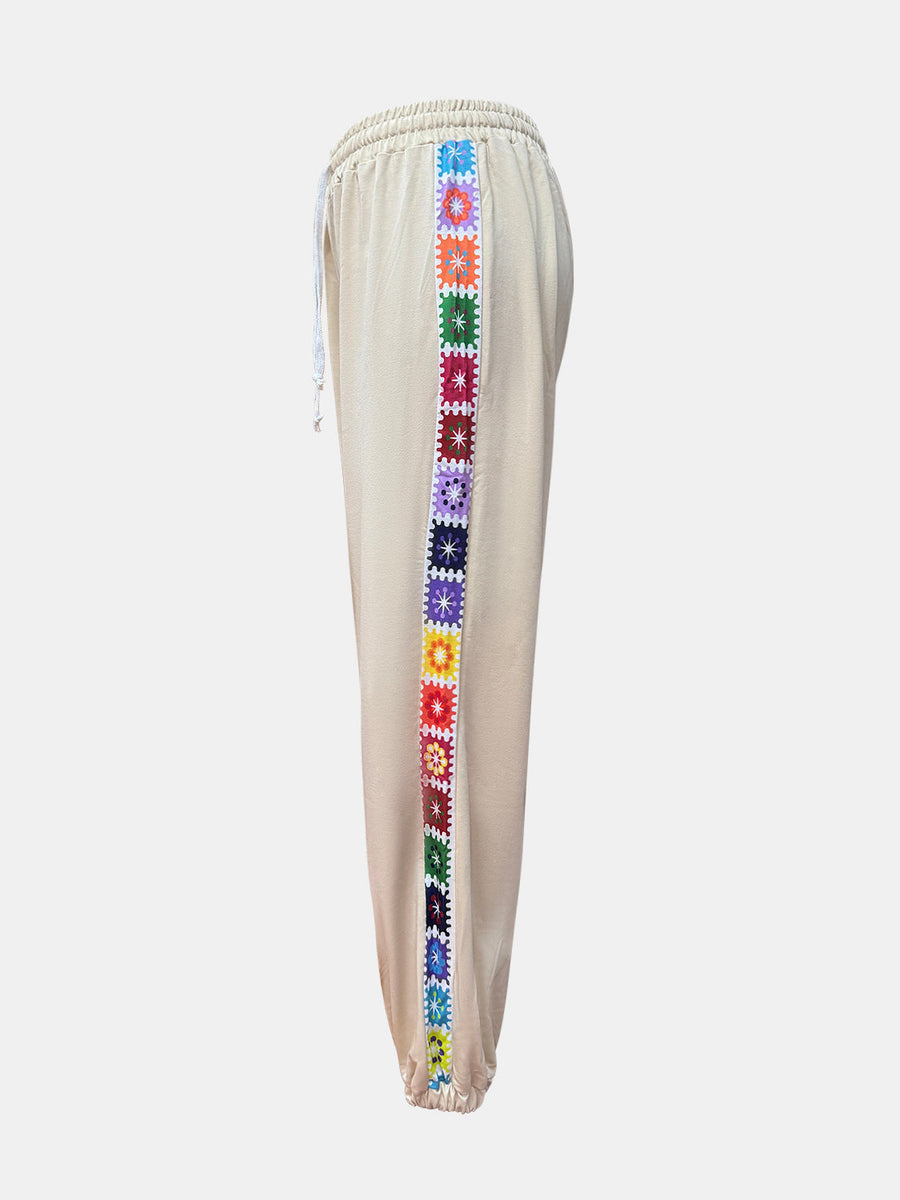 Tan jogger pants with colorful embroidered stripe detail down the side.