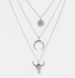 Silver layered pendant necklace with evil eye, crescent moon, and bull skull charms.