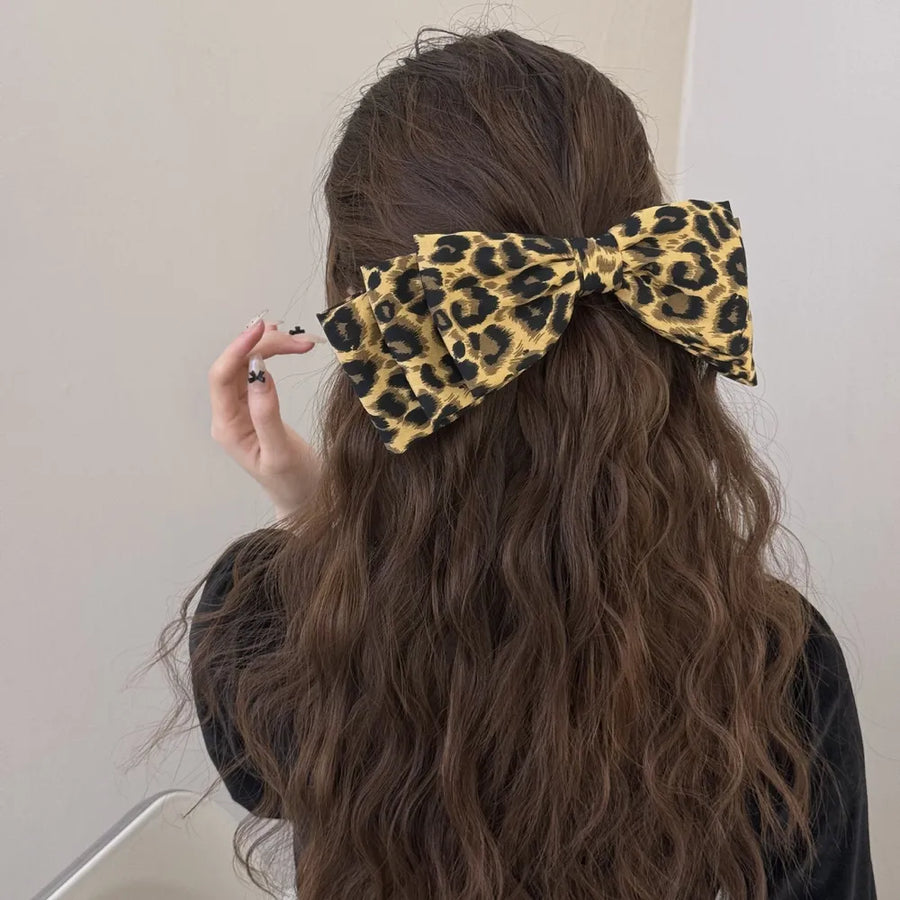 Leopard print oversized hair bow with fabric texture, worn in long wavy brown hair.