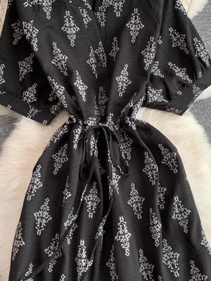 Black patterned drawstring jumpsuit with short puff sleeves and a tie waist.