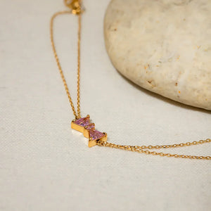 Gold chain bracelet with two pink gemstone bow charms.