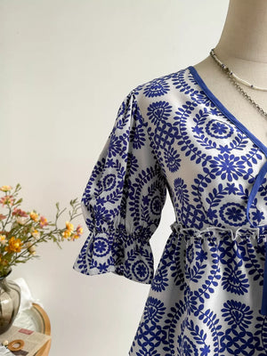 Chic floral tie-front blouse with 3/4 ruffled sleeves and blue floral print on white.