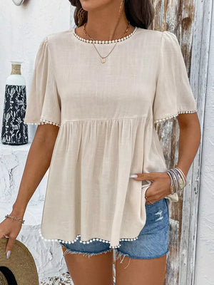 Charming babydoll blouse with pom-pom trim and short sleeves.