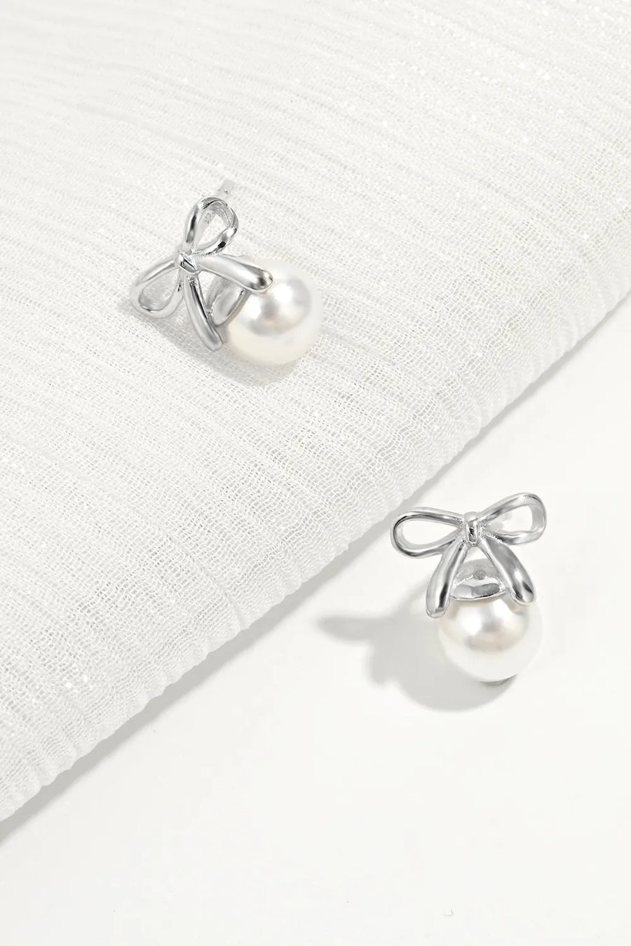 Silver bow pearl drop earrings with a classic pearl and delicate bow detail.
